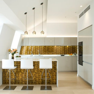 Medium sized contemporary galley kitchen in London with a submerged sink, flat-panel cabinets, beige cabinets, metallic splashback, black appliances, light hardwood flooring, a breakfast bar, beige floors and white worktops.