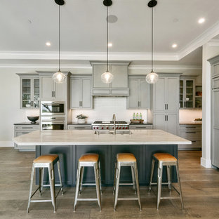 Foto di una cucina chic con lavello sottopiano, ante in stile shaker, ante grigie, paraspruzzi bianco, elettrodomestici da incasso, pavimento in legno massello medio, isola, pavimento marrone e top bianco