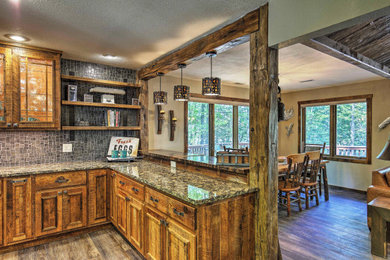 Mid-sized mountain style u-shaped vinyl floor and brown floor eat-in kitchen photo in Other with a farmhouse sink, raised-panel cabinets, distressed cabinets, granite countertops, gray backsplash, stone tile backsplash, stainless steel appliances, an island and multicolored countertops