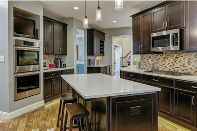 Large transitional medium tone wood floor kitchen photo in St Louis with an undermount sink, recessed-panel cabinets, dark wood cabinets, quartz countertops, multicolored backsplash, glass tile backsplash, stainless steel appliances and an island