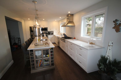 Example of a large transitional l-shaped dark wood floor and brown floor eat-in kitchen design in Toronto with a farmhouse sink, shaker cabinets, white cabinets, quartz countertops, white backsplash, mosaic tile backsplash, stainless steel appliances and an island
