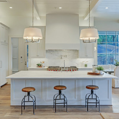 Example of a transitional l-shaped light wood floor and beige floor open concept kitchen design in Houston with recessed-panel cabinets, white cabinets, white backsplash, stone slab backsplash, an island and white countertops