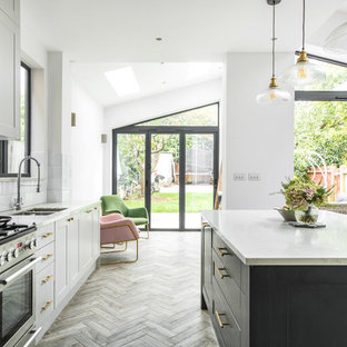 Photo of a traditional l-shaped kitchen in London with a double-bowl sink, shaker cabinets, white cabinets, white splashback, stainless steel appliances, medium hardwood flooring, an island, brown floors and white worktops.