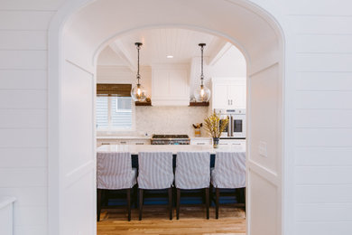 Example of a large beach style u-shaped medium tone wood floor, brown floor and shiplap ceiling eat-in kitchen design in Baltimore with a farmhouse sink, beaded inset cabinets, white cabinets, quartz countertops, white backsplash, quartz backsplash, stainless steel appliances, an island and white countertops
