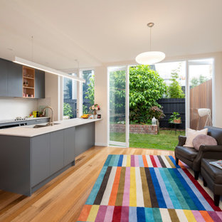Mid-sized contemporary galley open plan kitchen in Melbourne with a drop-in sink, flat-panel cabinets, grey cabinets, granite benchtops, white splashback, granite splashback, stainless steel appliances, medium hardwood floors, with island, brown floor and white benchtop.