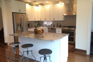 Example of a mid-sized trendy l-shaped medium tone wood floor eat-in kitchen design in New York with a farmhouse sink, shaker cabinets, white cabinets, granite countertops, gray backsplash, subway tile backsplash, stainless steel appliances and an island