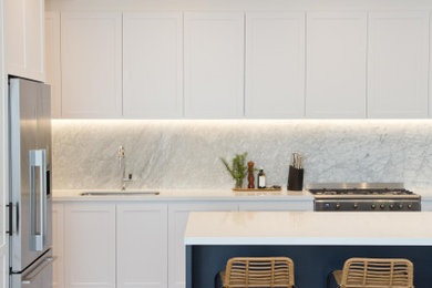 Inredning av ett modernt mellanstort vit vitt kök med öppen planlösning, med en nedsänkt diskho, skåp i shakerstil, vita skåp, bänkskiva i kvartsit, mellanmörkt trägolv och en köksö
