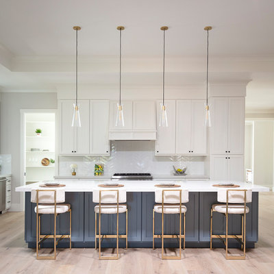 Example of a large farmhouse l-shaped light wood floor, gray floor and tray ceiling open concept kitchen design in San Francisco with a farmhouse sink, shaker cabinets, white cabinets, quartz countertops, white backsplash, ceramic backsplash, stainless steel appliances, an island and white countertops