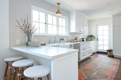 Inspiration for a medium sized coastal galley kitchen/diner in San Diego with a submerged sink, shaker cabinets, white cabinets, engineered stone countertops, grey splashback, ceramic splashback, stainless steel appliances, medium hardwood flooring, an island, brown floors and white worktops.