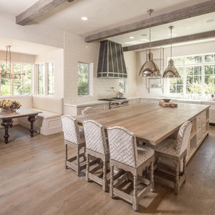 This is an example of a large shabby-chic style u-shaped eat-in kitchen in Houston with a farmhouse sink, shaker cabinets, white cabinets, solid surface benchtops, white splashback, ceramic splashback, stainless steel appliances, medium hardwood floors, with island and brown floor.