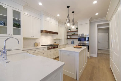 Klassisk inredning av ett mellanstort u-kök, med en rustik diskho, luckor med infälld panel, vita skåp, bänkskiva i kvarts, vitt stänkskydd, stänkskydd i keramik, rostfria vitvaror, mellanmörkt trägolv, en köksö och brunt golv