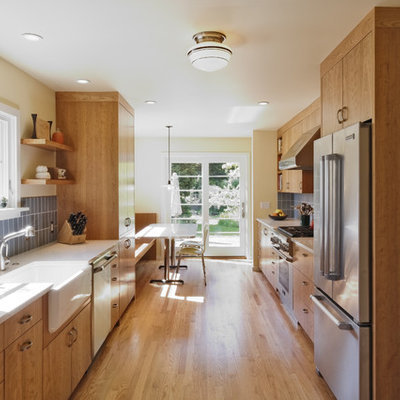 Transitional galley enclosed kitchen photo in Portland with a farmhouse sink, stainless steel appliances, flat-panel cabinets, medium tone wood cabinets, recycled glass countertops, blue backsplash and ceramic backsplash