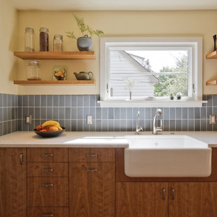 This is an example of a transitional galley eat-in kitchen in Portland with a farmhouse sink, blue splashback, flat-panel cabinets, medium wood cabinets, recycled glass benchtops, ceramic splashback and stainless steel appliances.