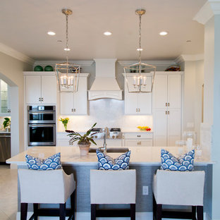 Photo of a large beach style u-shaped open plan kitchen in Miami with an integrated sink, shaker cabinets, white cabinets, granite benchtops, white splashback, stone slab splashback, stainless steel appliances, ceramic floors and a peninsula.