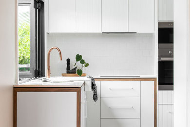 Inspiration for a scandinavian l-shaped kitchen in Hobart with a belfast sink, white cabinets, white splashback, ceramic splashback, stainless steel appliances, no island and white worktops.