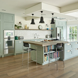 Inspiration for a large traditional open plan kitchen in London with shaker cabinets, stainless steel appliances, an island, white worktops, blue cabinets, white splashback, metro tiled splashback, light hardwood flooring and a single-bowl sink.