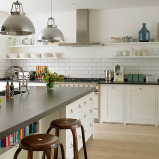 Inspiration for a mid-sized transitional u-shaped eat-in kitchen in London with white cabinets, white splashback, subway tile splashback, a drop-in sink, shaker cabinets, limestone benchtops, panelled appliances, light hardwood floors, with island, beige floor and grey benchtop.