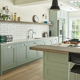 Large transitional single-wall open plan kitchen in London with a drop-in sink, shaker cabinets, green cabinets, quartzite benchtops, white splashback, subway tile splashback, stainless steel appliances, with island and white benchtop.