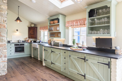 Ejemplo de cocina de estilo de casa de campo sin isla con fregadero sobremueble, puertas de armario verdes, electrodomésticos negros, suelo de madera en tonos medios y suelo marrón