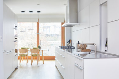 This is an example of a medium sized scandi galley kitchen/diner in Toronto with a submerged sink, flat-panel cabinets, white cabinets, engineered stone countertops, white splashback, stainless steel appliances, light hardwood flooring, no island, brown floors and grey worktops.