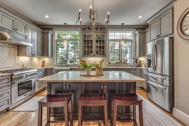 Kitchen - mid-sized traditional u-shaped light wood floor and beige floor kitchen idea in Boston with a farmhouse sink, raised-panel cabinets, gray cabinets, granite countertops, ceramic backsplash, stainless steel appliances, an island and multicolored backsplash
