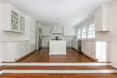 Große Klassische Wohnküche in U-Form mit Schrankfronten im Shaker-Stil, weißen Schränken, Küchenrückwand in Weiß, Küchengeräten aus Edelstahl, braunem Holzboden und Kücheninsel in Charleston