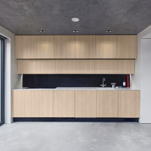 This is an example of a small contemporary single-wall kitchen in London with a submerged sink, flat-panel cabinets, black splashback, integrated appliances, concrete flooring, no island, grey floors, light wood cabinets and white worktops.