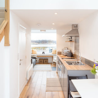 Photo of a small coastal galley open plan kitchen in Other with a single-bowl sink, shaker cabinets, grey cabinets, wood worktops, metallic splashback, integrated appliances, medium hardwood flooring, no island and brown worktops.