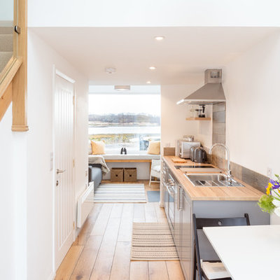 Example of a small beach style galley medium tone wood floor open concept kitchen design in Other with a single-bowl sink, shaker cabinets, gray cabinets, wood countertops, metallic backsplash, paneled appliances, no island and brown countertops
