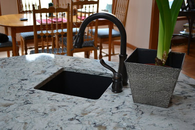 Foto de cocina tradicional renovada de tamaño medio con fregadero bajoencimera, encimera de granito, electrodomésticos negros, suelo de madera clara y una isla