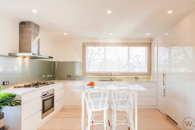 Inredning av ett modernt stort kök, med en nedsänkt diskho, släta luckor, vita skåp, bänkskiva i kvarts, stänkskydd i glaskakel, rostfria vitvaror och en köksö