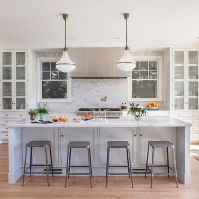 Example of a mid-sized transitional l-shaped light wood floor eat-in kitchen design in Los Angeles with an undermount sink, glass-front cabinets, white cabinets, marble countertops, white backsplash, stone slab backsplash, stainless steel appliances and an island