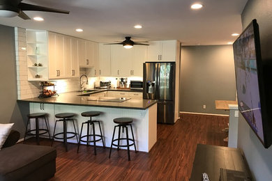 Inspiration for a large transitional u-shaped dark wood floor and brown floor open concept kitchen remodel in Hawaii with an undermount sink, shaker cabinets, white cabinets, white backsplash, subway tile backsplash, stainless steel appliances, a peninsula, black countertops and solid surface countertops