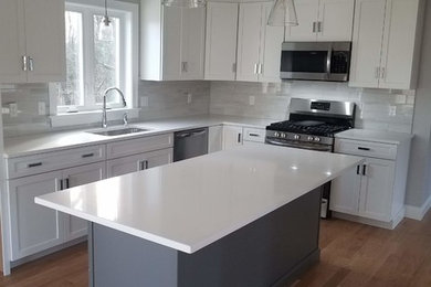 Medium sized modern l-shaped kitchen/diner in Providence with a submerged sink, shaker cabinets, white cabinets, engineered stone countertops, white splashback, ceramic splashback, stainless steel appliances, medium hardwood flooring, an island, beige floors and white worktops.