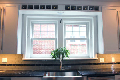 フィラデルフィアにある高級な広いトランジショナルスタイルのおしゃれなキッチン (エプロンフロントシンク、シェーカースタイル扉のキャビネット、白いキャビネット、クオーツストーンカウンター、ベージュキッチンパネル、ガラスタイルのキッチンパネル、シルバーの調理設備、ラミネートの床、黒い床) の写真