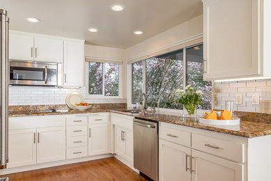 Inspiration for a mid-sized timeless galley light wood floor enclosed kitchen remodel in San Francisco with an undermount sink, shaker cabinets, white cabinets, granite countertops, beige backsplash, glass tile backsplash, stainless steel appliances and no island