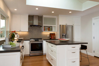 Example of a mid-sized trendy l-shaped medium tone wood floor eat-in kitchen design in San Francisco with an undermount sink, recessed-panel cabinets, white cabinets, quartz countertops, gray backsplash, glass tile backsplash, stainless steel appliances and an island