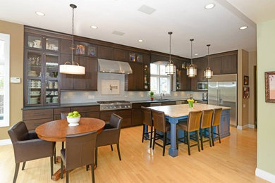 Example of a mid-sized classic l-shaped light wood floor and beige floor eat-in kitchen design in Chicago with shaker cabinets, dark wood cabinets, gray backsplash, subway tile backsplash, stainless steel appliances and an island