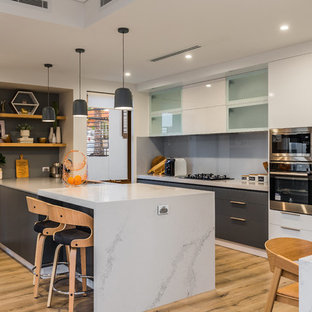 This is an example of a contemporary eat-in kitchen in Perth with flat-panel cabinets, grey cabinets, grey splashback, glass sheet splashback, stainless steel appliances, light hardwood floors, a peninsula, beige floor and grey benchtop.