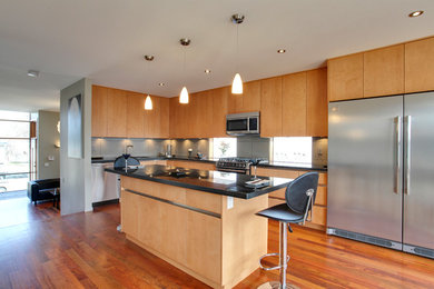 Example of a large minimalist l-shaped light wood floor and brown floor eat-in kitchen design in Calgary with an undermount sink, flat-panel cabinets, light wood cabinets, solid surface countertops, gray backsplash, porcelain backsplash, stainless steel appliances and an island