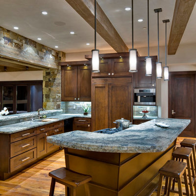 Inspiration for a large rustic medium tone wood floor eat-in kitchen remodel in Denver with an undermount sink, recessed-panel cabinets, dark wood cabinets, granite countertops, gray backsplash, stone tile backsplash, stainless steel appliances and an island