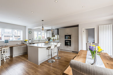 Inspiration for a medium sized classic open plan kitchen in Surrey with shaker cabinets, beige cabinets, quartz worktops, black appliances, an island and white worktops.