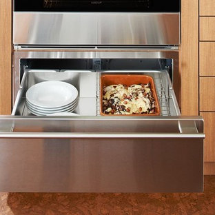Foto de cocina de galera, moderna, de tamaño medio, abierta, con armarios con paneles lisos, puertas de armario de madera oscura, encimera de acrílico, electrodomésticos de acero inoxidable, suelo de corcho, una isla y suelo marrón
