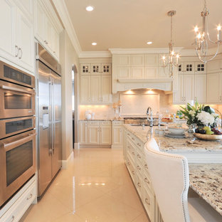 This is an example of a large traditional u-shaped open plan kitchen in Edmonton with beige splashback, stainless steel appliances, with island, an undermount sink, recessed-panel cabinets, white cabinets, granite benchtops, stone tile splashback and marble floors.