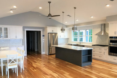 Example of a large transitional l-shaped medium tone wood floor and brown floor eat-in kitchen design in Portland Maine with an undermount sink, beaded inset cabinets, white cabinets, quartzite countertops, gray backsplash, porcelain backsplash, stainless steel appliances and an island