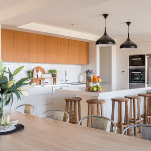 Contemporary l-shaped eat-in kitchen in Sydney with medium wood cabinets, white splashback, with island, white benchtop, flat-panel cabinets, subway tile splashback, stainless steel appliances, light hardwood floors and beige floor.