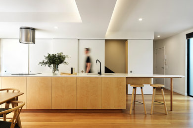 Idée de décoration pour une cuisine design en bois clair avec un évier 2 bacs, un placard à porte plane, un sol en bois brun, îlot, un sol marron et un plan de travail blanc.