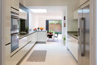 ロンドンにある中くらいなコンテンポラリースタイルのおしゃれなキッチン (ダブルシンク、フラットパネル扉のキャビネット、白いキャビネット、御影石カウンター、ガラス板のキッチンパネル、白い調理設備) の写真
