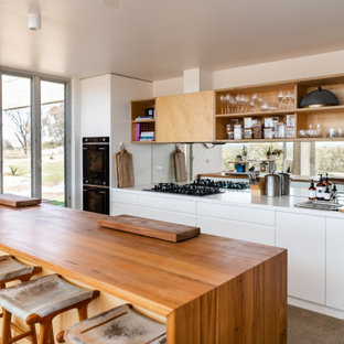 Design ideas for a mid-sized contemporary galley open plan kitchen in Other with a double-bowl sink, white cabinets, wood benchtops, metallic splashback, mirror splashback, white appliances, concrete floors, with island, grey floor, brown benchtop and flat-panel cabinets.