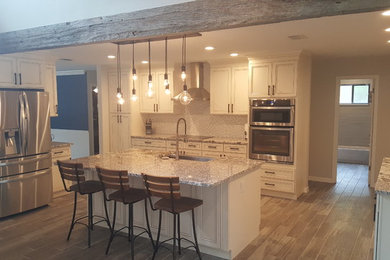 Example of a large transitional u-shaped medium tone wood floor and brown floor eat-in kitchen design in Orlando with a farmhouse sink, recessed-panel cabinets, white cabinets, granite countertops, glass sheet backsplash, stainless steel appliances, an island, white backsplash and multicolored countertops